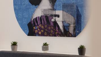 A wall-mounted artwork depicting a woman with flowers, a bed with red and white pillows, and two potted plants.