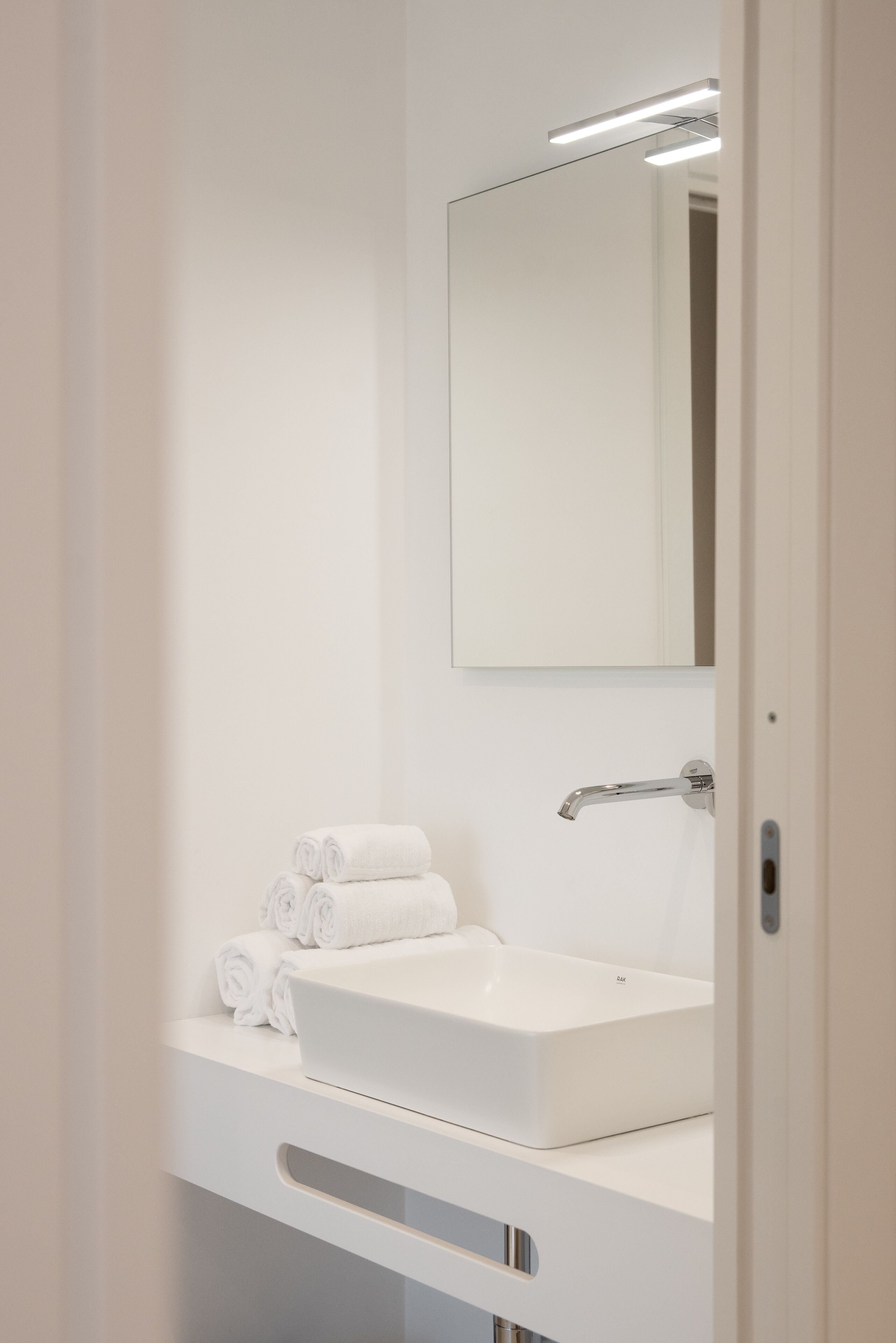 Ein modernes Badezimmer mit einem weißen Waschbecken, einem Spiegel und ordentlich gefalteten Handtüchern.