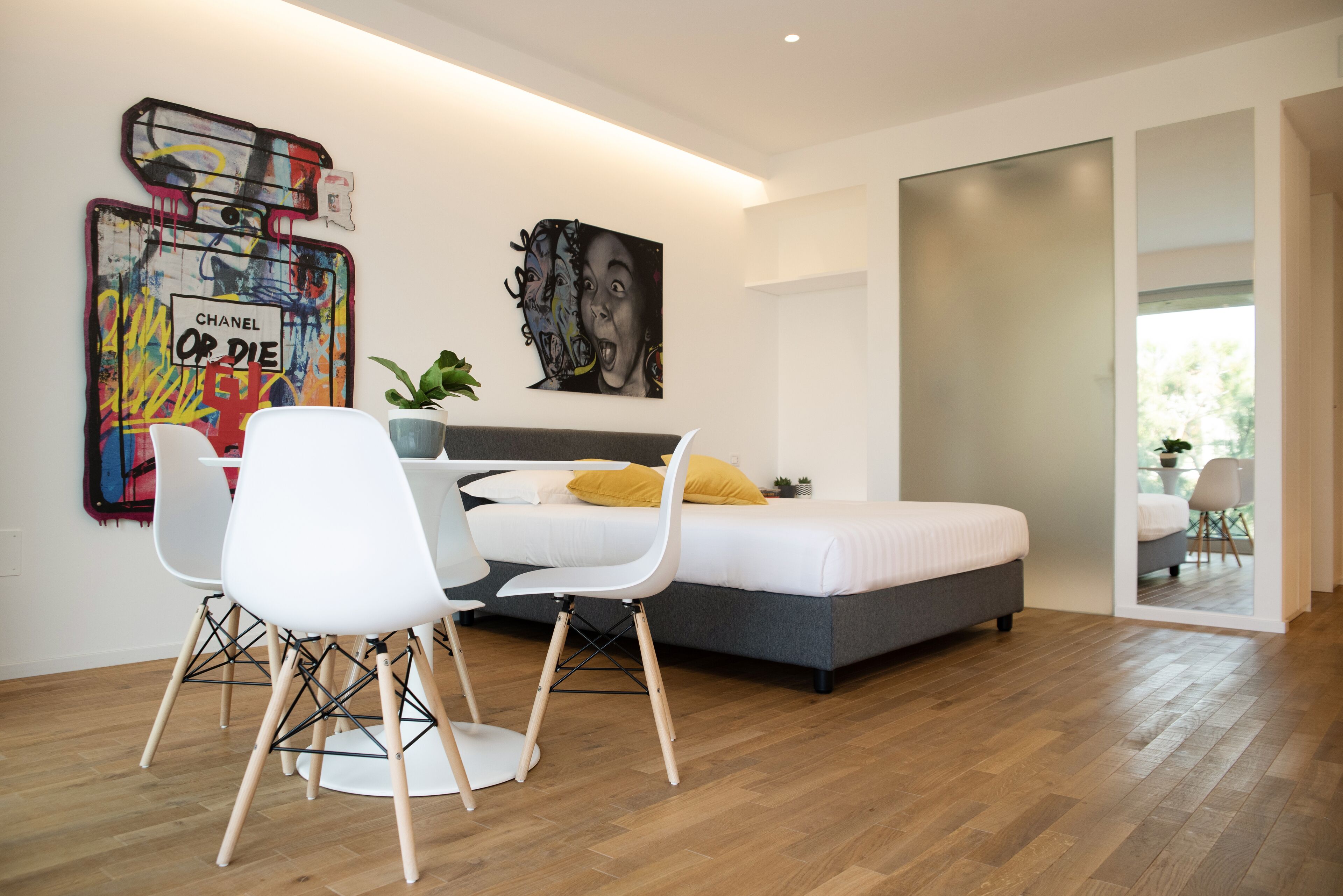 Une chambre moderne avec un lit, un bureau avec des chaises et des œuvres d’art accrochées aux murs.