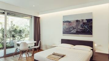 A modern bedroom with a large bed, a dining table with chairs, a small side table, and a large window with curtains.