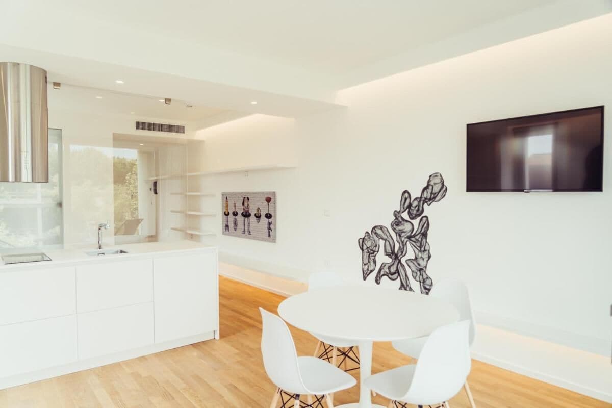A modern kitchen with white cabinetry, a built-in stove, and a dining area with a white table and chairs.