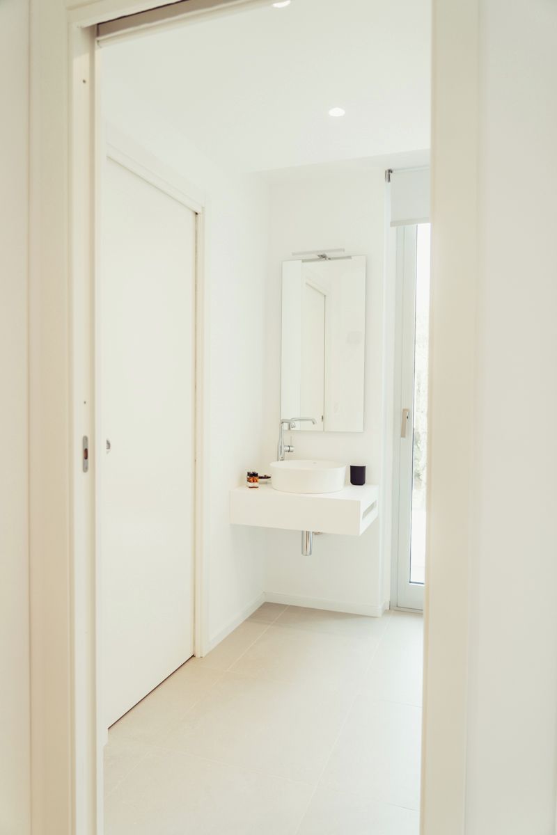 A modern bathroom with a white sink, mirror, and a door leading to another room.