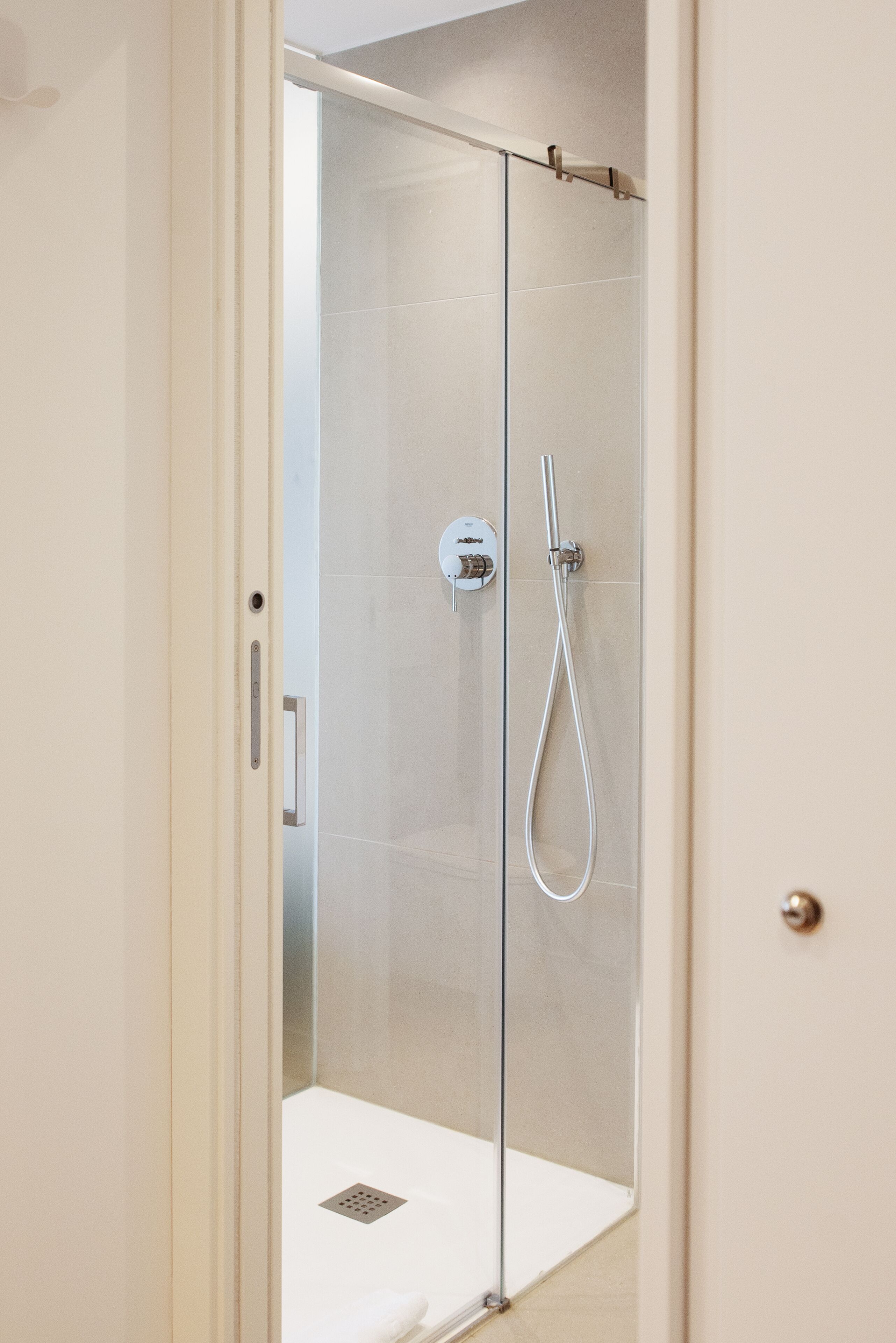 Una ducha con cerramiento de vidrio, cabezal de ducha manual y panel de control en la pared.