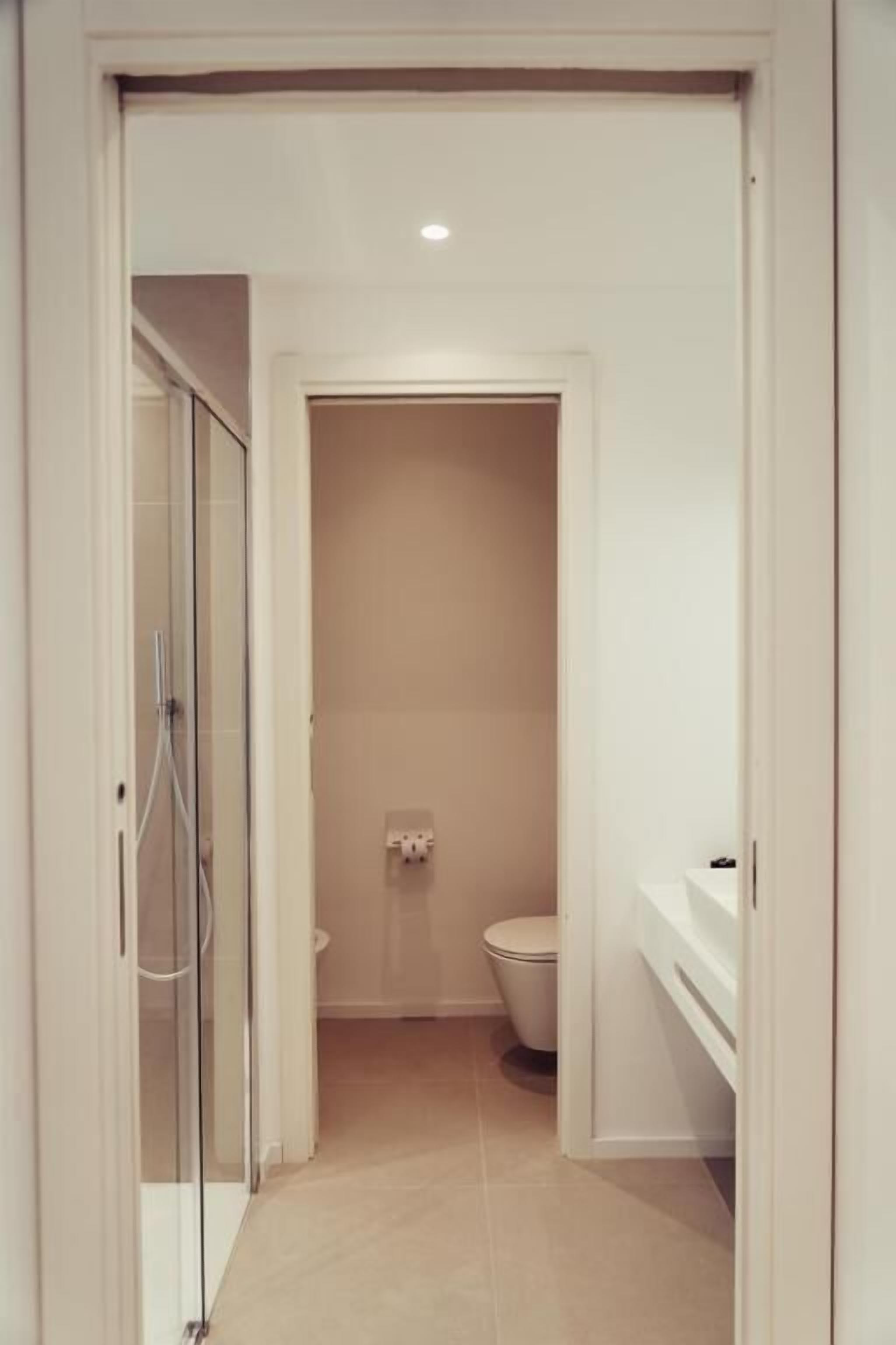 Ein schmaler Flur, der zu einem Badezimmer mit Toilette und Duschbereich führt.