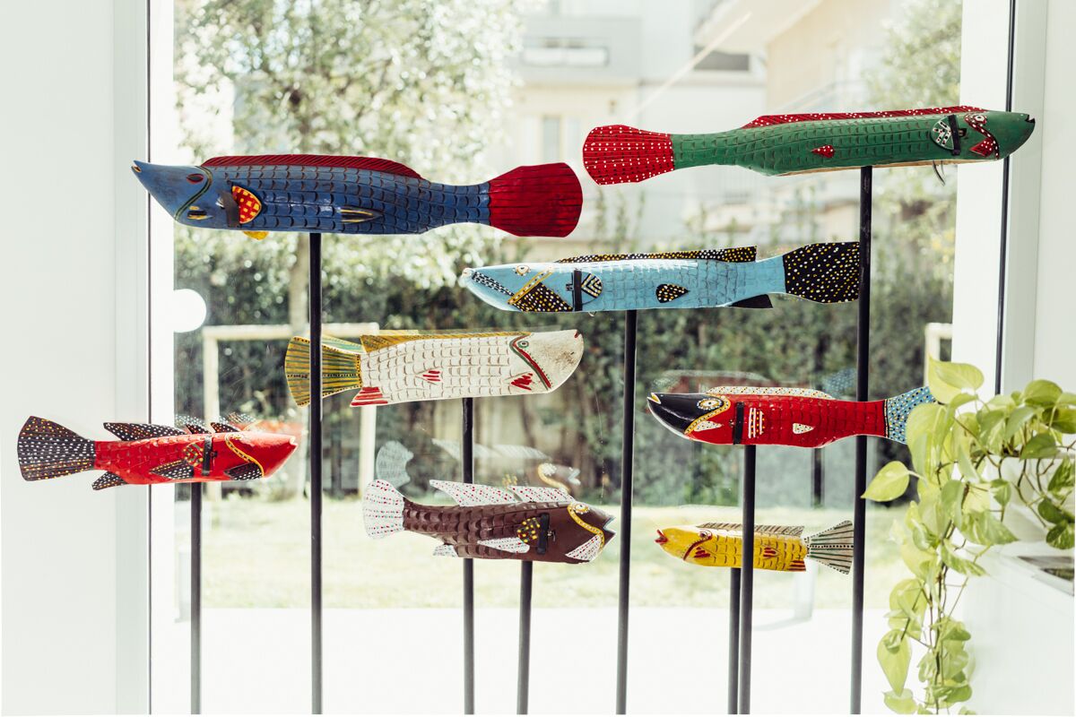 Un grupo de decoraciones con forma de pez, de colores variados, colgando de una ventana.