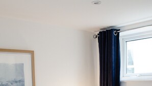 Habitación de hotel con cama, mesita de noche con lámpara, un cuadro enmarcado en la pared y ventana con cortinas.