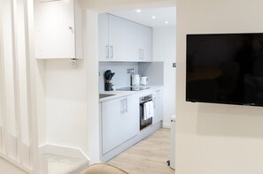 Une cuisine moderne avec des meubles blancs, un four encastré et un téléviseur à écran plat fixé au mur.