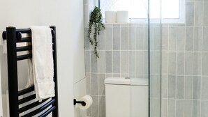 Un baño con ducha envuelta en vidrio, inodoro, toallero y ventana.