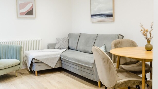 Una sala de estar moderna con un sofá gris, una mesa redonda de madera y un radiador.