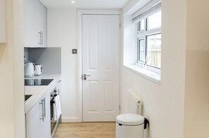 Une cuisine étroite avec des meubles blancs, une porte blanche, une fenêtre donnant sur un paysage agréable et un radiateur blanc.