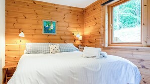 A wooden-paneled bedroom with a bed, pillows, a nightstand, a lamp, and a window with a view of trees. - 2 bedroom accommodation in Linlithgow, near Edinburgh (Linlithgow, near Edinburgh)