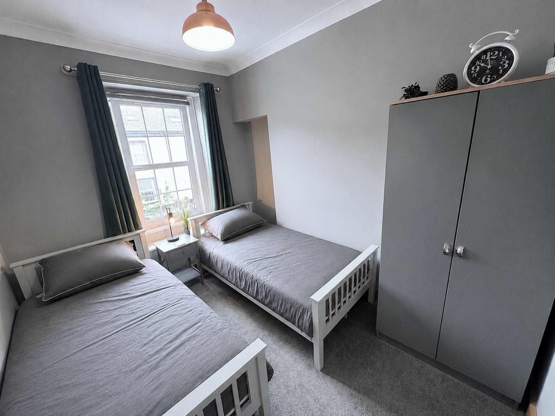 A bedroom with two single beds, a wardrobe, a window with curtains, and a bedside lamp.