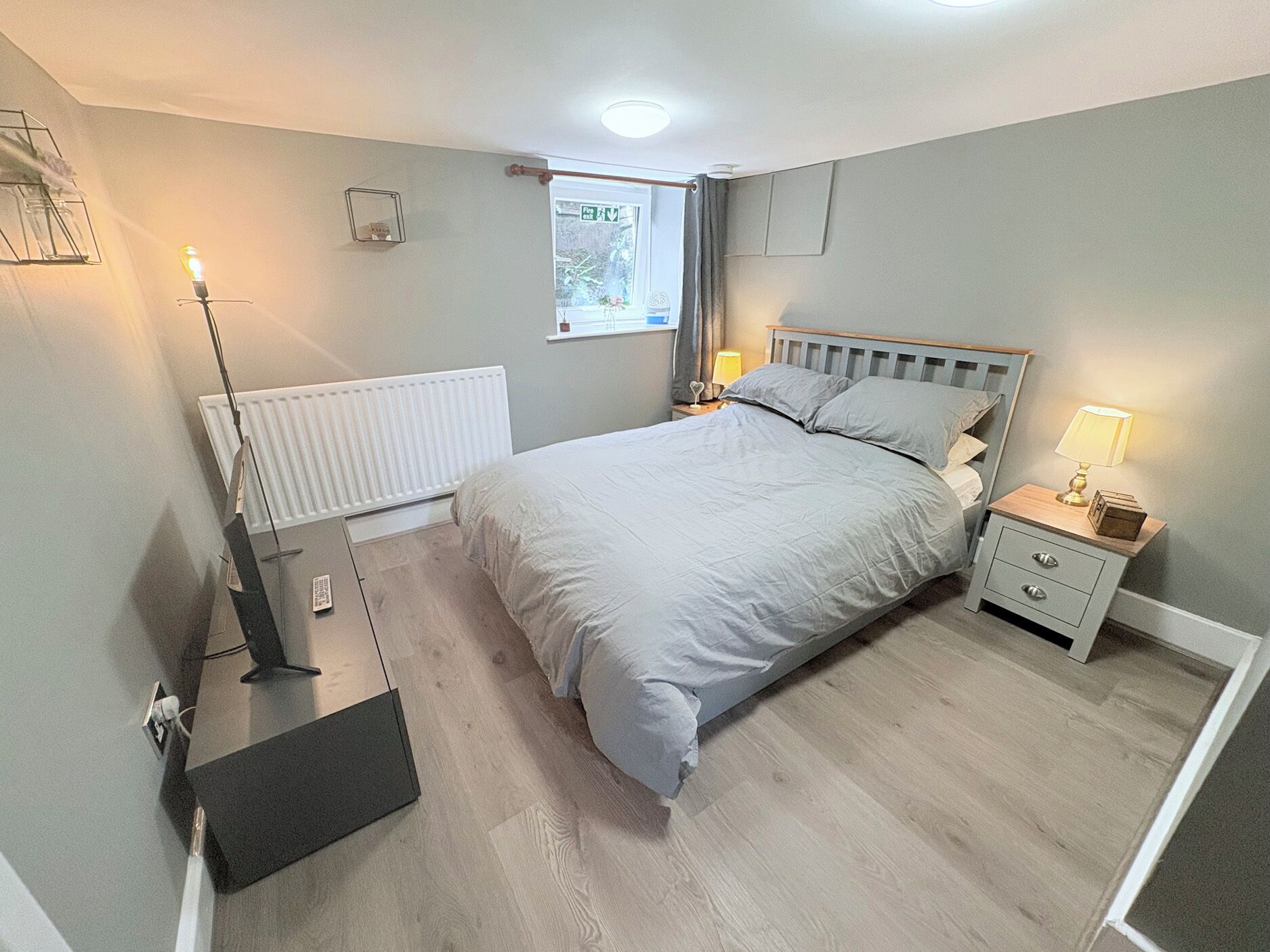 A bedroom with a bed, bedside tables, a radiator, a window, and a door.
