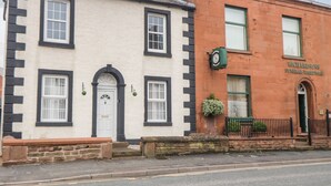 A two-story building with a white facade and black trim, featuring a green clock and a sign for Richardsons Funeral Directors. - The Oaks Cottage (Penrith)