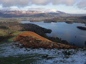 A panoramic view of a mountainous landscape with a lake, forested hills, and a small town in the valley. - The Oaks Cottage (Penrith)