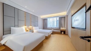 A hotel room with two beds, a desk, a TV, and a large window.