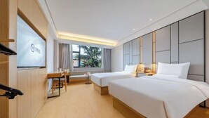 A hotel room with two beds, a desk, a TV, and a window with a view.
