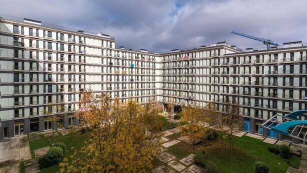Un edificio moderno de varios pisos con un patio central, balcones y una grúa de construcción al fondo.