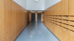 Un pasillo con taquillas de madera y suelo azul, que conduce a la zona de ascensores.