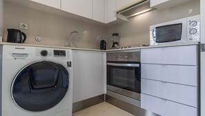 Una cocina compacta equipada con lavadora, horno, microondas y cafetera.