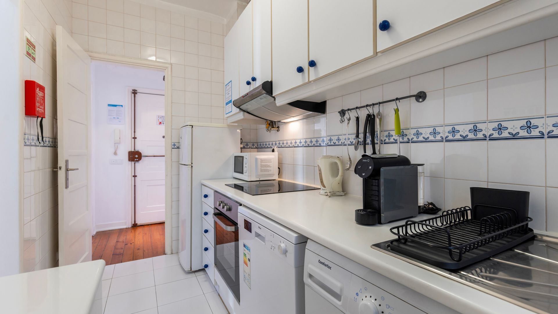 A compact kitchen with white cabinets, a dishwasher, a coffee machine, and a kettle.