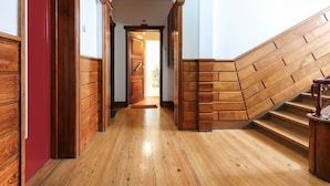 Una escalera de madera con barandilla, suelo de madera y una puerta que da a otra habitación.