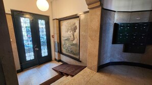 Un vestíbulo con una puerta negra con paneles de vidrio, un mural de un paisaje, un banco y un buzón fijado a la pared.