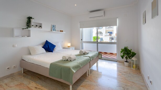 Une chambre à coucher moderne avec un lit, des tables de chevet, une fenêtre et une vue sur l’extérieur.