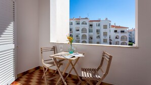 Un balcon avec une table, deux chaises, un vase de fleurs et une vue sur des bâtiments blancs aux toits rouges.