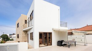 Une maison moderne à deux étages, dotée d’un balcon, d’une porte-fenêtre coulissante et d’un petit patio avec une table et des chaises.