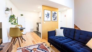 A modern living room with a blue sofa, a dining area with a table and chairs, and a kitchen in the background.