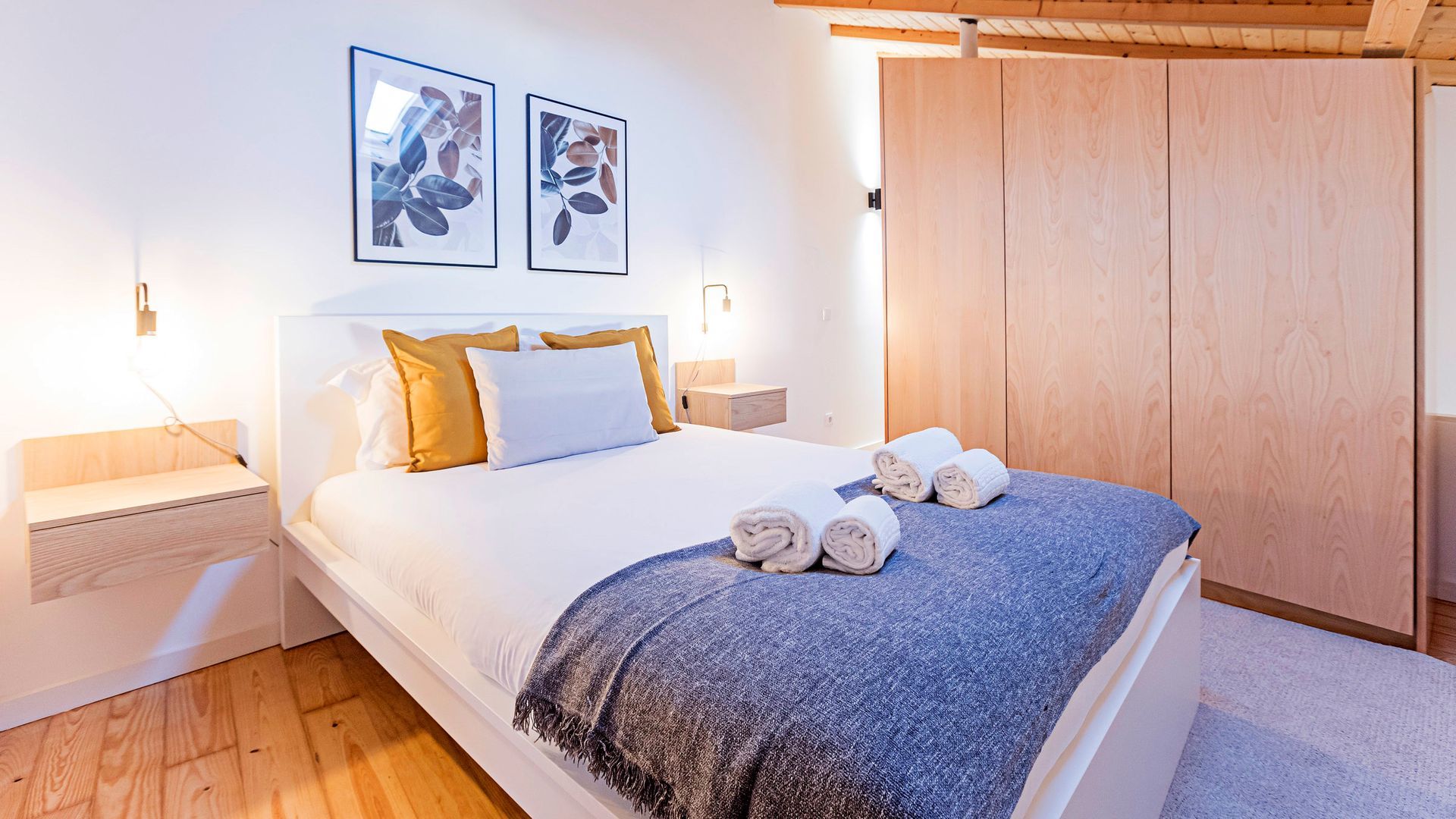 A bedroom with a bed, a wooden wardrobe, and two framed pictures on the wall.