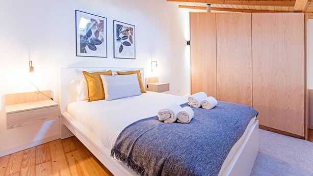 A bedroom with a bed, a wooden wardrobe, and two framed pictures on the wall.