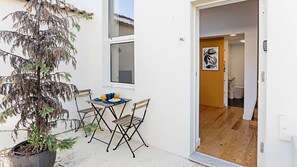 Ein kleiner Außenbereich mit Tisch und Stühlen, einem Blumentopf und einem Fenster.