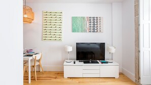 A modern living room with a white TV stand, a flat-screen TV, two wall-mounted lamps, and a wicker light fixture.
