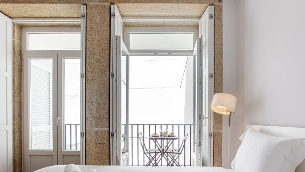 Una habitación de hotel con una cama, un balcón con mesa y sillas, y una lámpara.