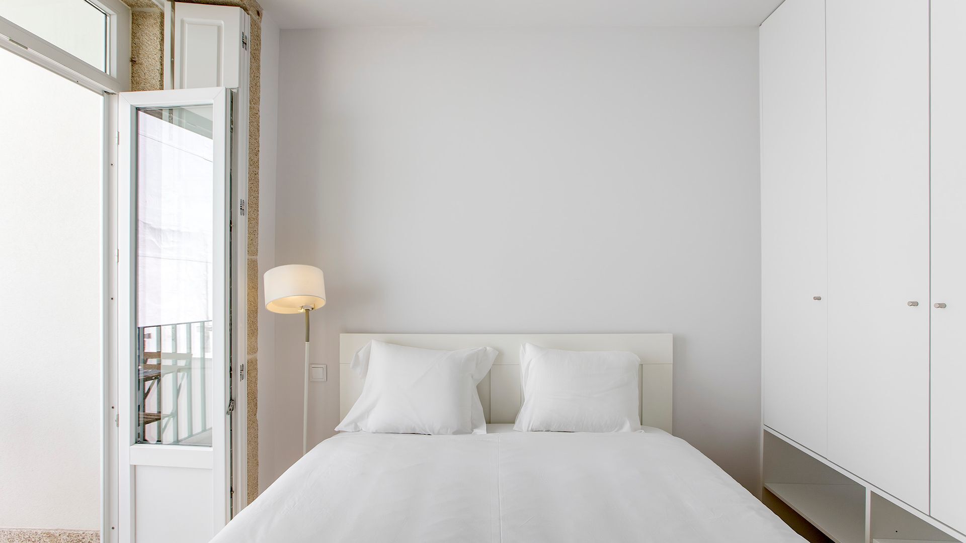 A bedroom with a bed, a nightstand, a lamp, and a wardrobe.