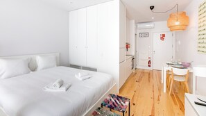 A modern hotel room with a large bed, a small kitchenette, a dining area, and a bathroom.