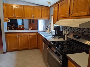 Una cocina con armarios de madera, estufa, pileta y cafetera.