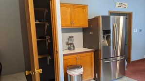 A kitchen with wooden cabinets, a stainless steel refrigerator, a blender, and a trash can. - Hackert Lake House near Ludington! (Scottville)