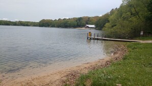 A lakeside view with a dock extending into the water, surrounded by grassy areas and trees. - Hackert Lake House near Ludington! (Scottville)