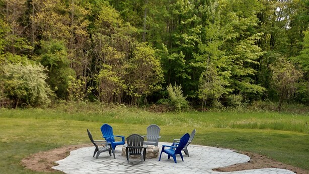 A paved patio with hexagonal tiles, surrounded by a grassy area with trees. - Hackert Lake House near Ludington! (Scottville)