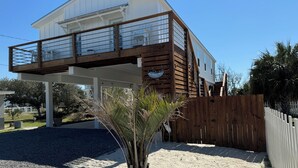 A two-story house with a balcony, a wooden fence, and a palm tree in the foreground. - Family Fun only steps away from Saint Joe Beach! Gulf Views!! Swim Spa 15ftx7ft! (Port St. Joe)