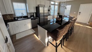 A modern kitchen with white cabinets, a black island, and a woven chair. - Family Fun only steps away from Saint Joe Beach! Gulf Views!! Swim Spa 15ftx7ft! (Port St. Joe)