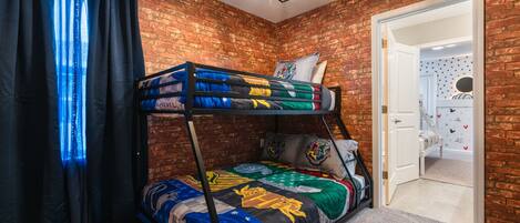 A bunk bed with a colorful quilt, a brick wall, a door with a polka dot pattern, and a chandelier.