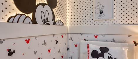 Una habitación con papel tapiz de Mickey Mouse, un gran recorte de Mickey Mouse y una almohada con Mickey Mouse.