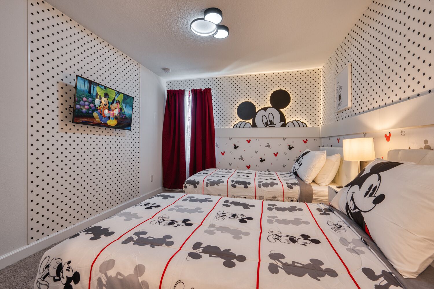 Ein Zimmer mit zwei Betten, beide mit Bettwäsche im Mickey-Mouse-Design. An der Wand hängt ein Bild und über den Betten befinden sich Mickey-Mouse-Kopfstücke.