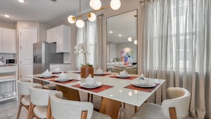 Un comedor moderno con una gran mesa rectangular, sillas blancas y un florero central.