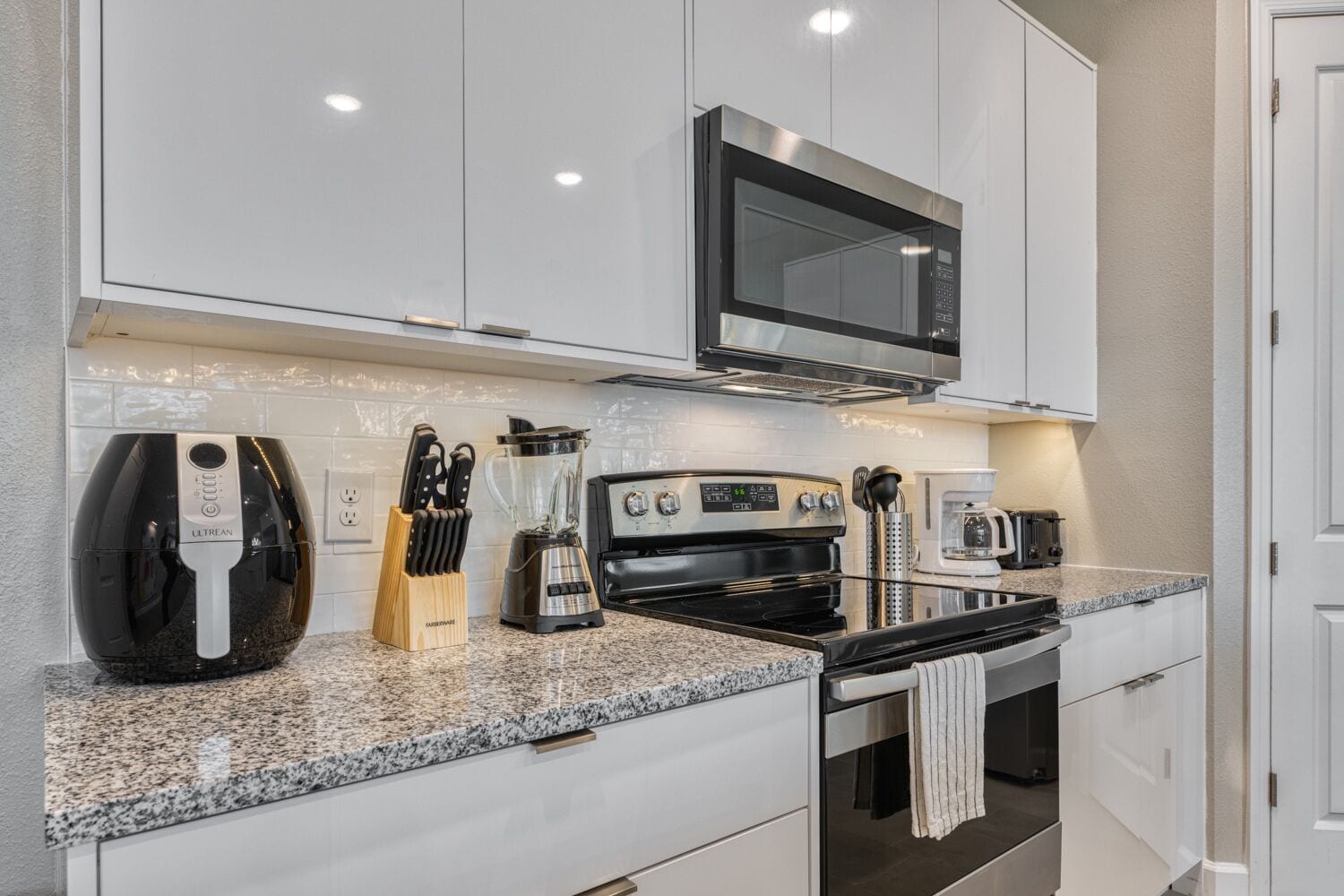 A modern kitchen with white cabinets, a stainless steel microwave, a black stove, and a coffee maker.
