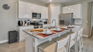 Una cocina moderna con armarios blancos, encimera de granito y una isla central con sillas.